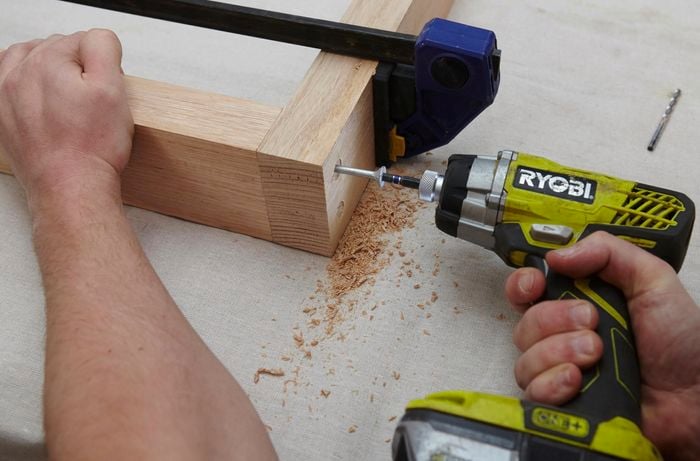 A wooden frame to be used as dining table legs being assembled with a power drill, screws and a clamp