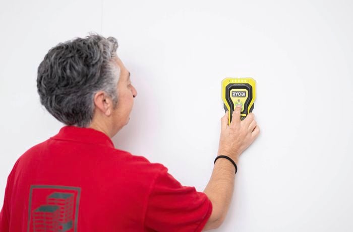 A Bunnings Team Member is using a stud finder to locate the wall studs before the Ryobi LINK rail installation.  