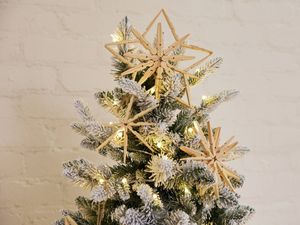 Handmade star ornaments crafted from wooden pegs hanging on a Christmas tree with fairy lights.