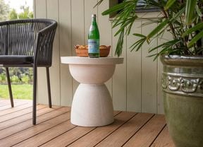 An outdoor white colour side table with a rounded surface and a bottle sitting on top of it.