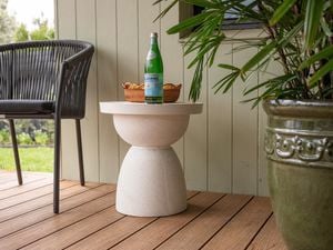 An outdoor white colour side table with a rounded surface and a bottle sitting on top of it.