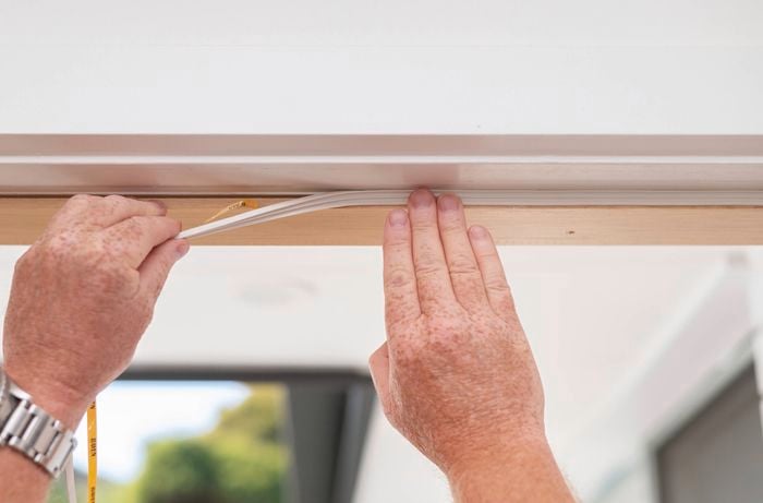 A person is using both hands to apply a weather strip, holding and pressing it into place.