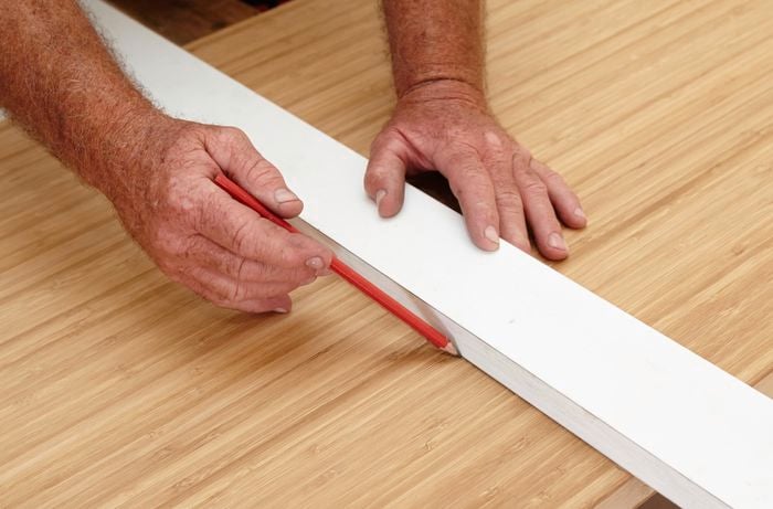 Person measuring and marking cut to be made on benchtop