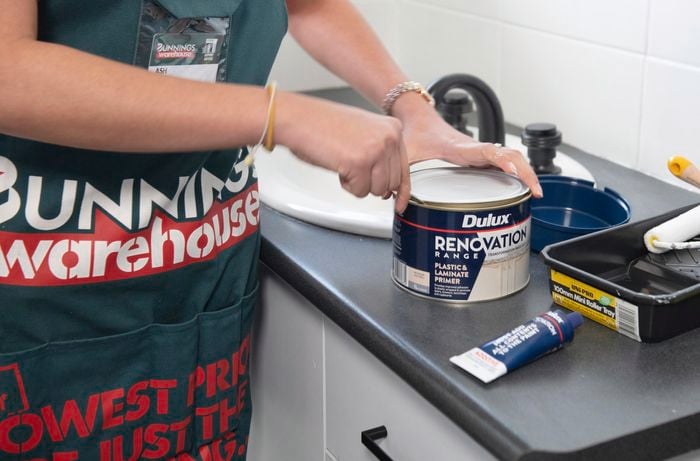 A person opening a tin of Dulux plastic and laminate primer