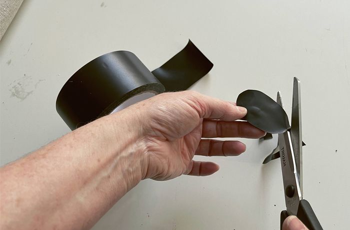 Hands cutting black duct tape into an oval shape with scissors.