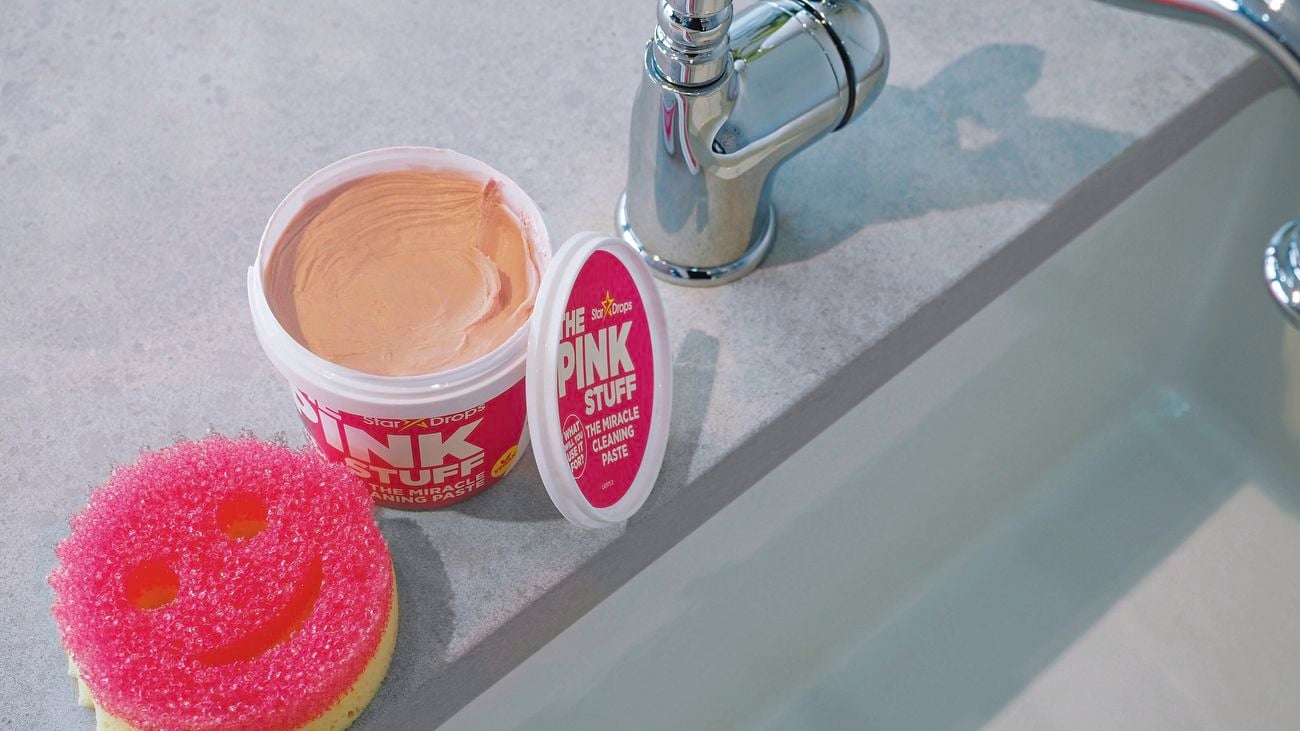 Tub of pink cleaning paste sitting next to scourer in shape of smiling face.