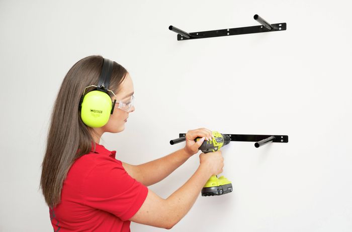 Person wearing hearing protection while drilling into a wall at a marked stud location.