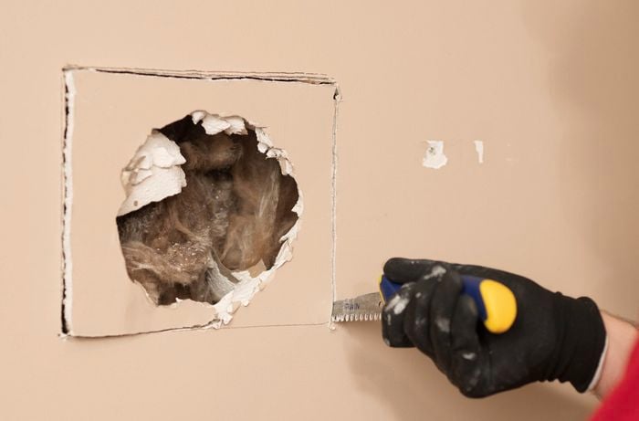 A person wearing gloves is using a jab saw to cut plasterboard along the traced line.