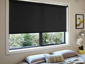 A black roller blind installed in a window in a light themed bedroom