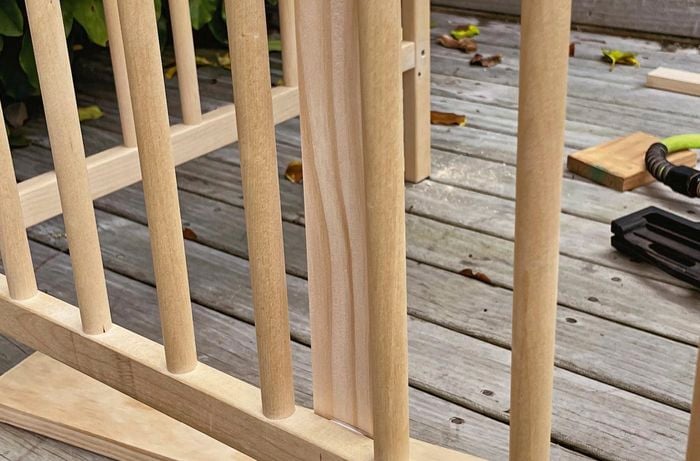 Close up of wooden cot railings with a piece of wood behind