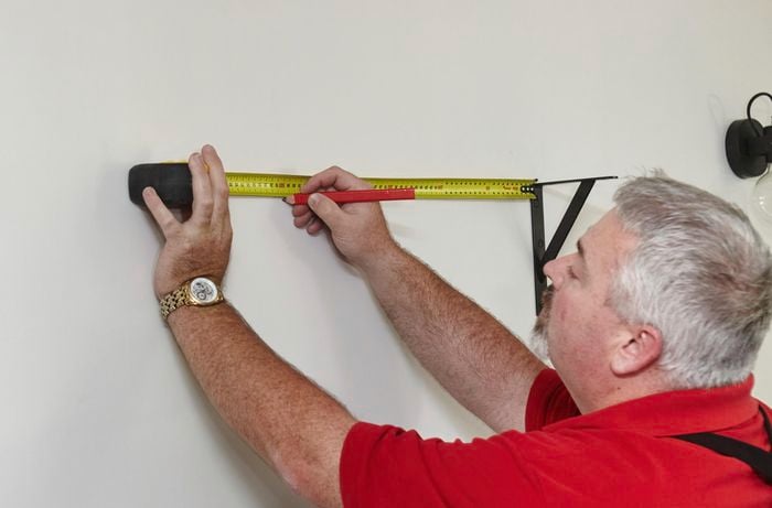 A person marking a wall using a measuring tape