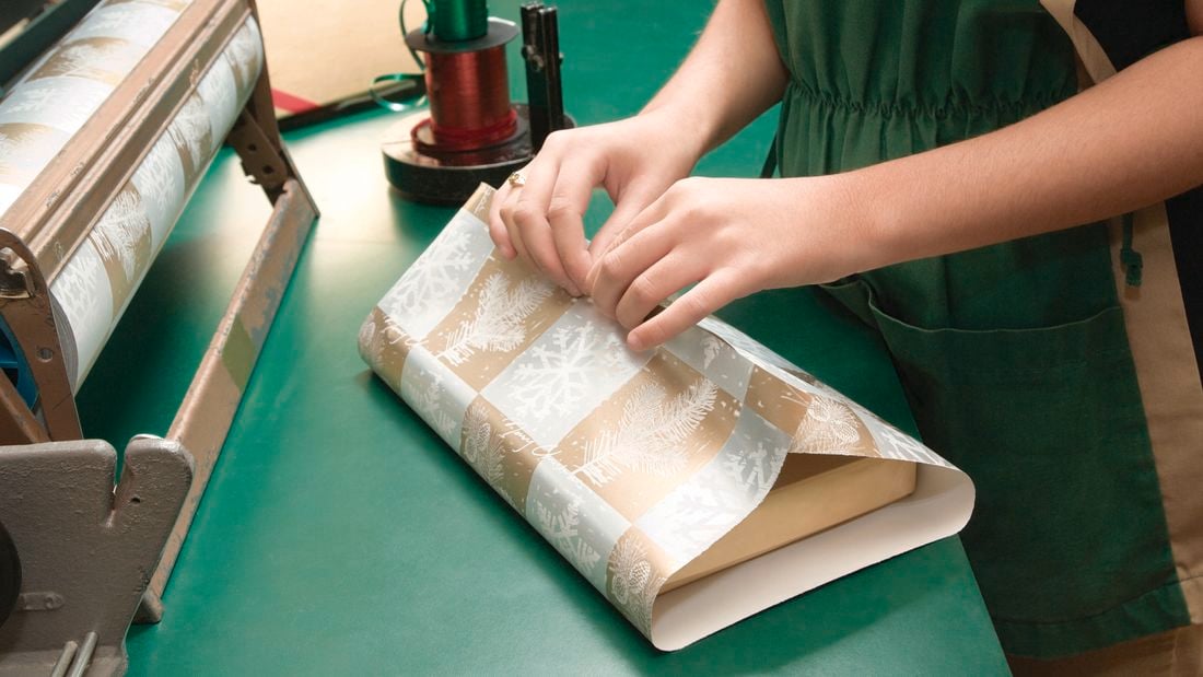 Person wrapping gift in gold and silver wrapping paper.