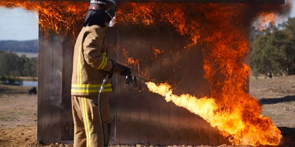 Person in protective wear testing FIRECOAT on a small structure.