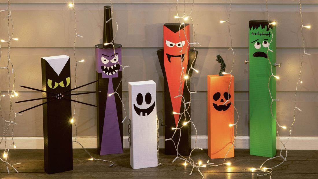 Halloween decorations made from painted rectangular blocks, including a cat, witch, ghost, vampire, pumpkin, and Frankenstein's monster, surrounded by string lights.