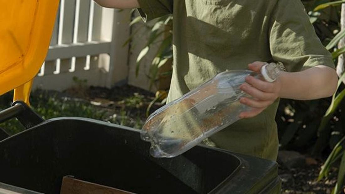 Person placing a plastic bottle in a recycling bin