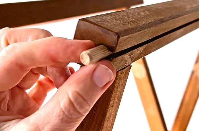 Close up of a hand pushing a small fluted dowel into the end of a wooden frame