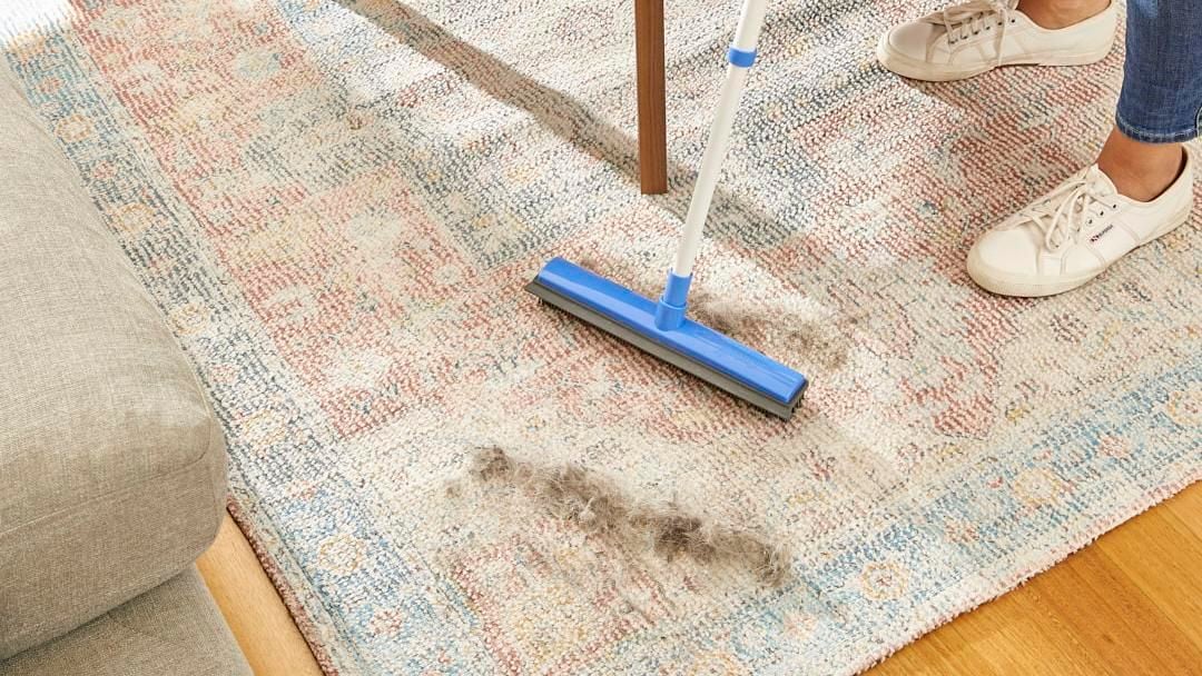 Person using broom to clear dust of rug