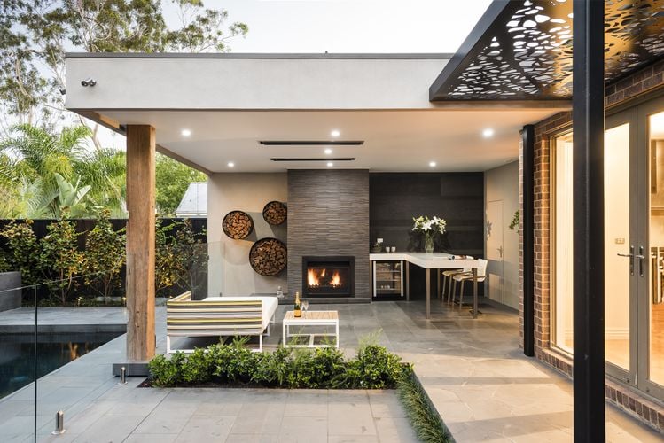 Outdoor lounge area with lounge and coffee table heated by roof mounted heat lamps and fireplace