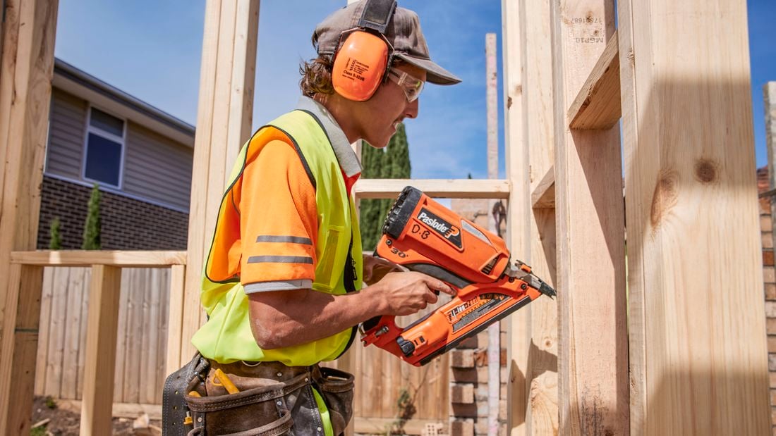 A tradie uses a Paslode nail gun on a frame wearing hearing protection