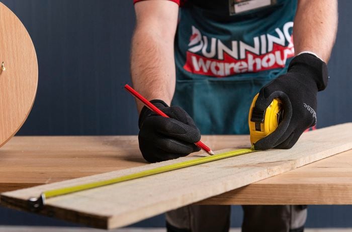 Using a tape measure with a pencil marking out measurements on fence paling.