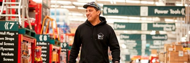 customers walking through a Bunnings store,  carrying a bunnings shopping basket with items in it.