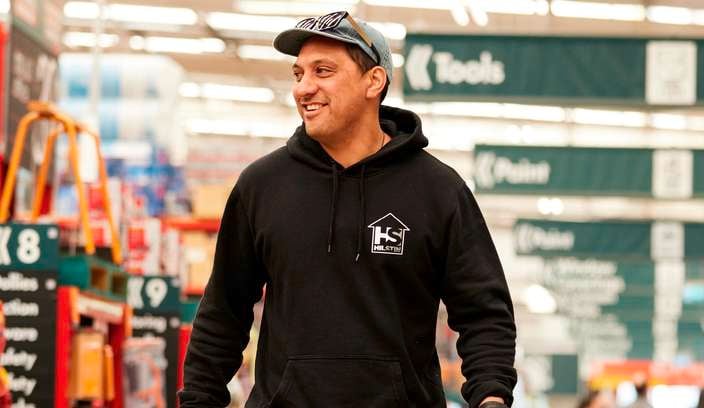 customers walking through a Bunnings store,  carrying a bunnings shopping basket with items in it.