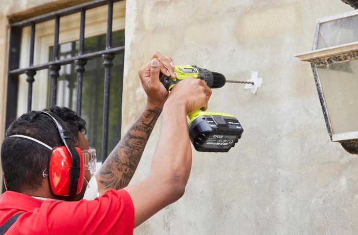 Person wearing safety glasses and earmuffs drilling a marked hole into a wall