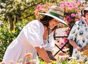 Katie of Little Lyndoch Flower Farm and her mother wear sunhats while gardening outdoors among pink and orange flowers.