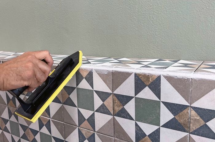 A close up of a hand applying grout to tiles with a grout float