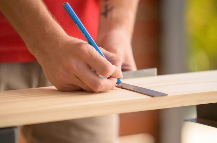 A person is measuring and marking on a wooden board with a ruler and pencil to make a bookshelf.