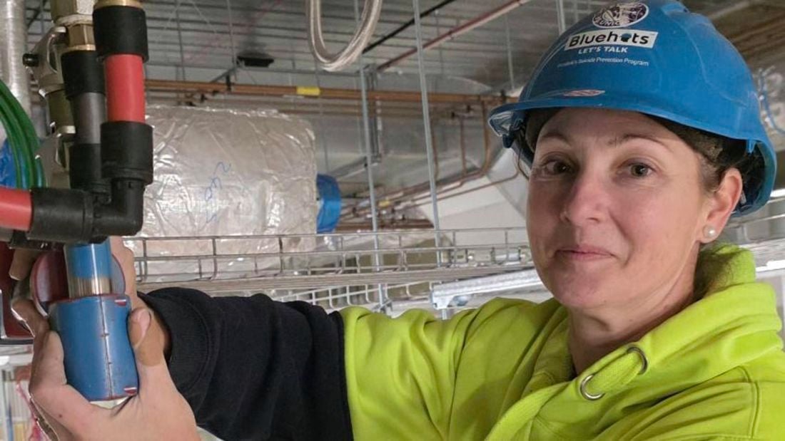: A female plumber wearing yellow hi-vis and a blue helmet while fitting REHAU pipes.