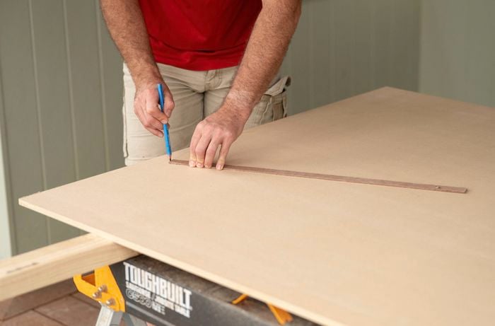 A person is using a pencil and a straight edge to mark measurements on a MDF.