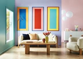 Living room with a cream colour sofa, three colourful rectangular painted wall panels on a purple wall, a tan coffee table and a cream colour bean shaped sofa chair