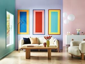 Living room with a cream colour sofa, three colourful rectangular painted wall panels on a purple wall, a tan coffee table and a cream colour bean shaped sofa chair