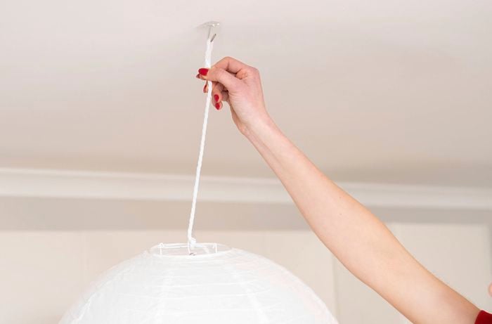 A person is hanging a DIY pendant light rope to a ceiling adhesive hook.