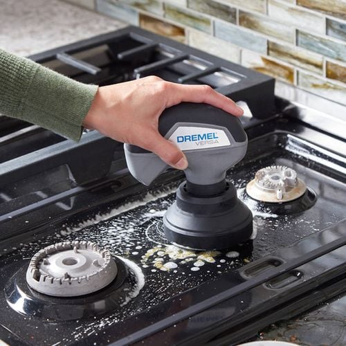 Hand using Dremel Versa scrubber to clean a stovetop.