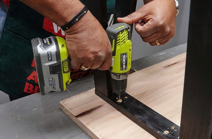 A person drilling into table legs on an inverted table