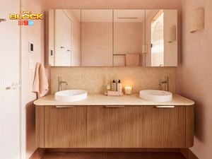 Modern bathroom with double round sinks, chrome faucets, mirrored cabinets, soft pink walls, and toiletries on the vanity. 