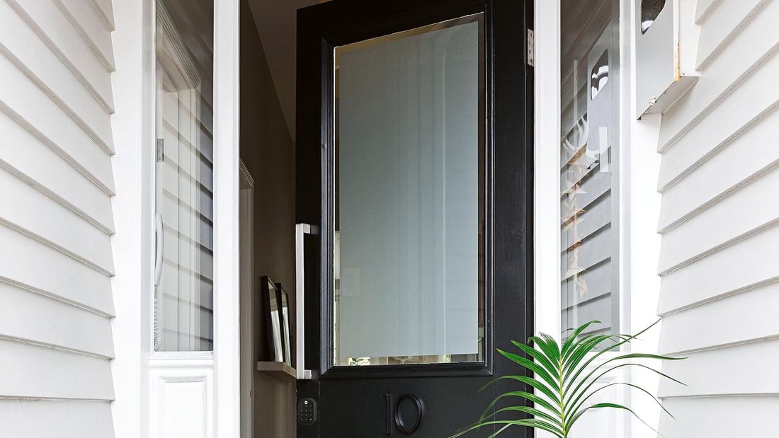 Black front entry door of a home featuring a frosted glass panel and a smart door lock.