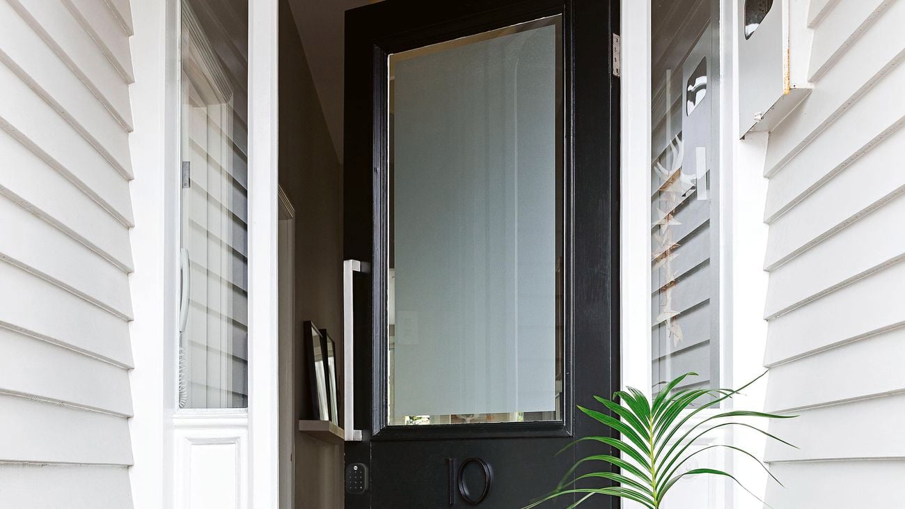 Black front entry door of a home featuring a frosted glass panel and a smart door lock.