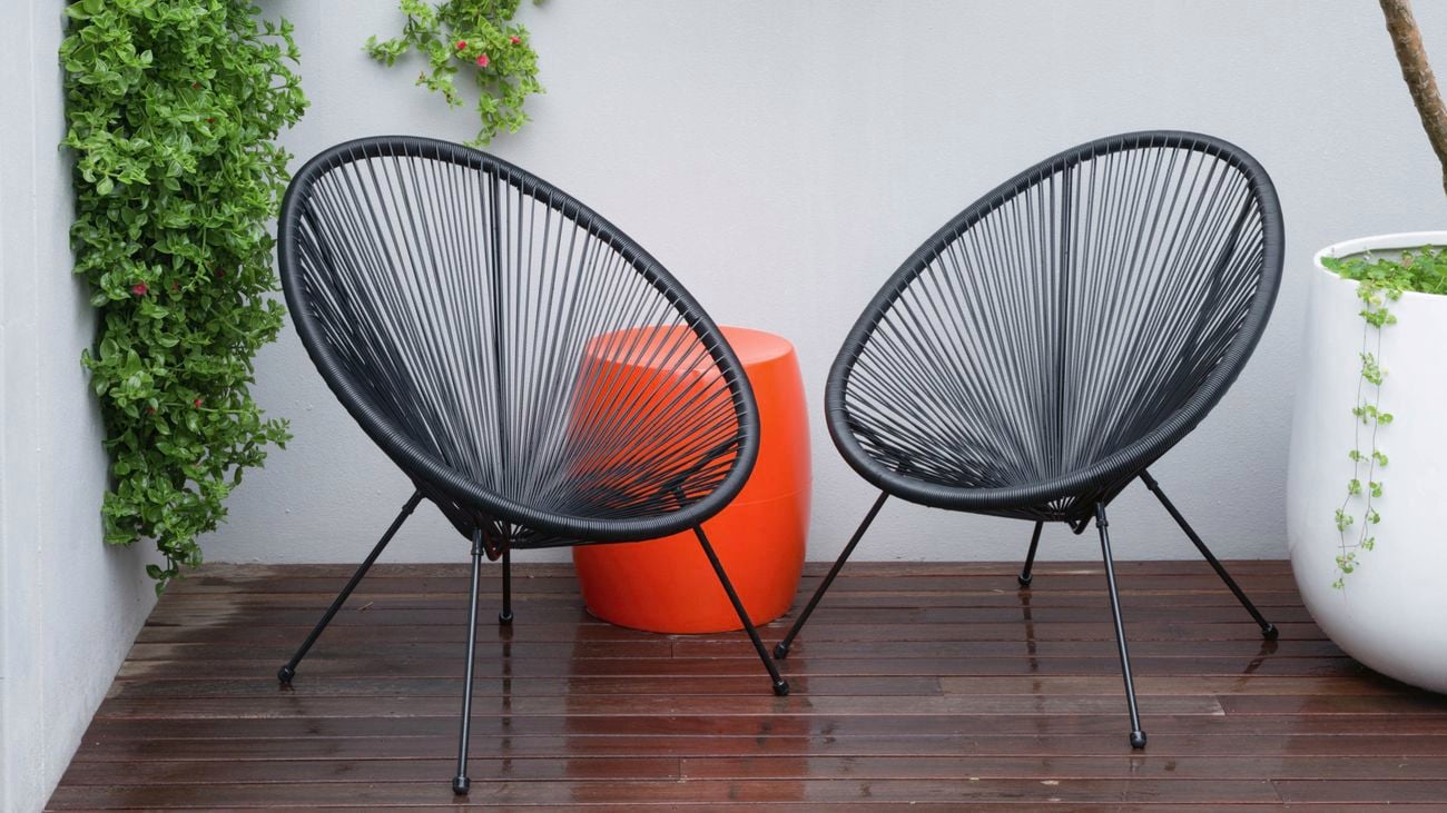 Two black verna acapulco chairs sit opposite eachother on a wooden deck in a small courtyard