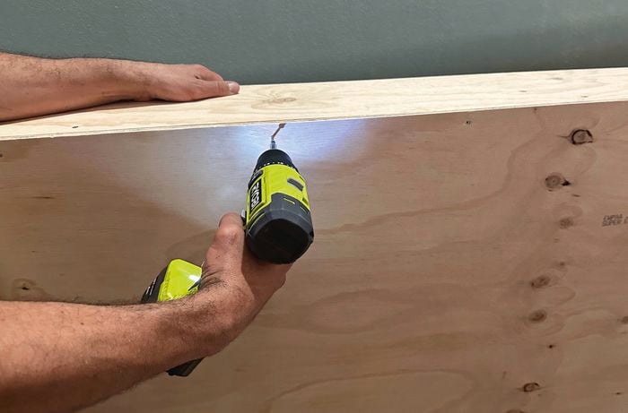 A close up of of a hand using a drill on plywood to make the bedhead