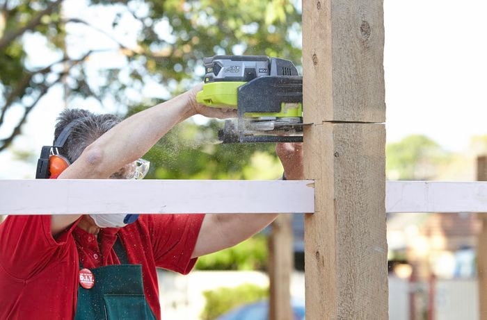 A Bunnings team member cutting the top from an upright fence post using a circular saw