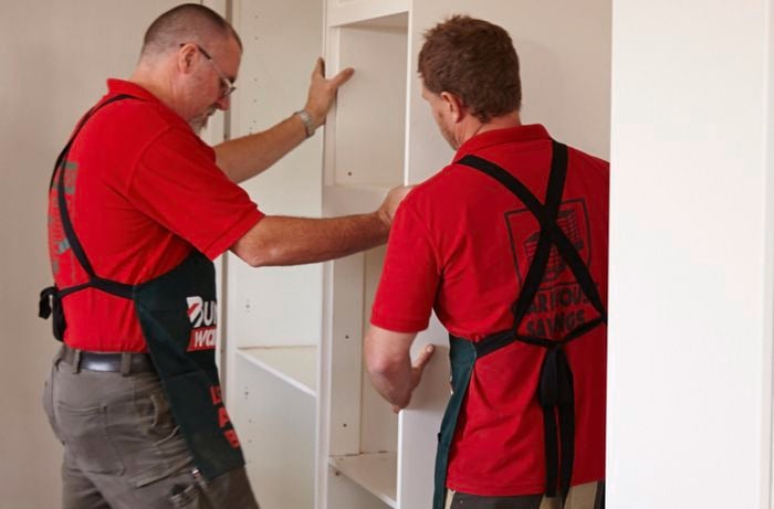 A kitchen pantry unit being positioned against a wall by two Bunnings team members