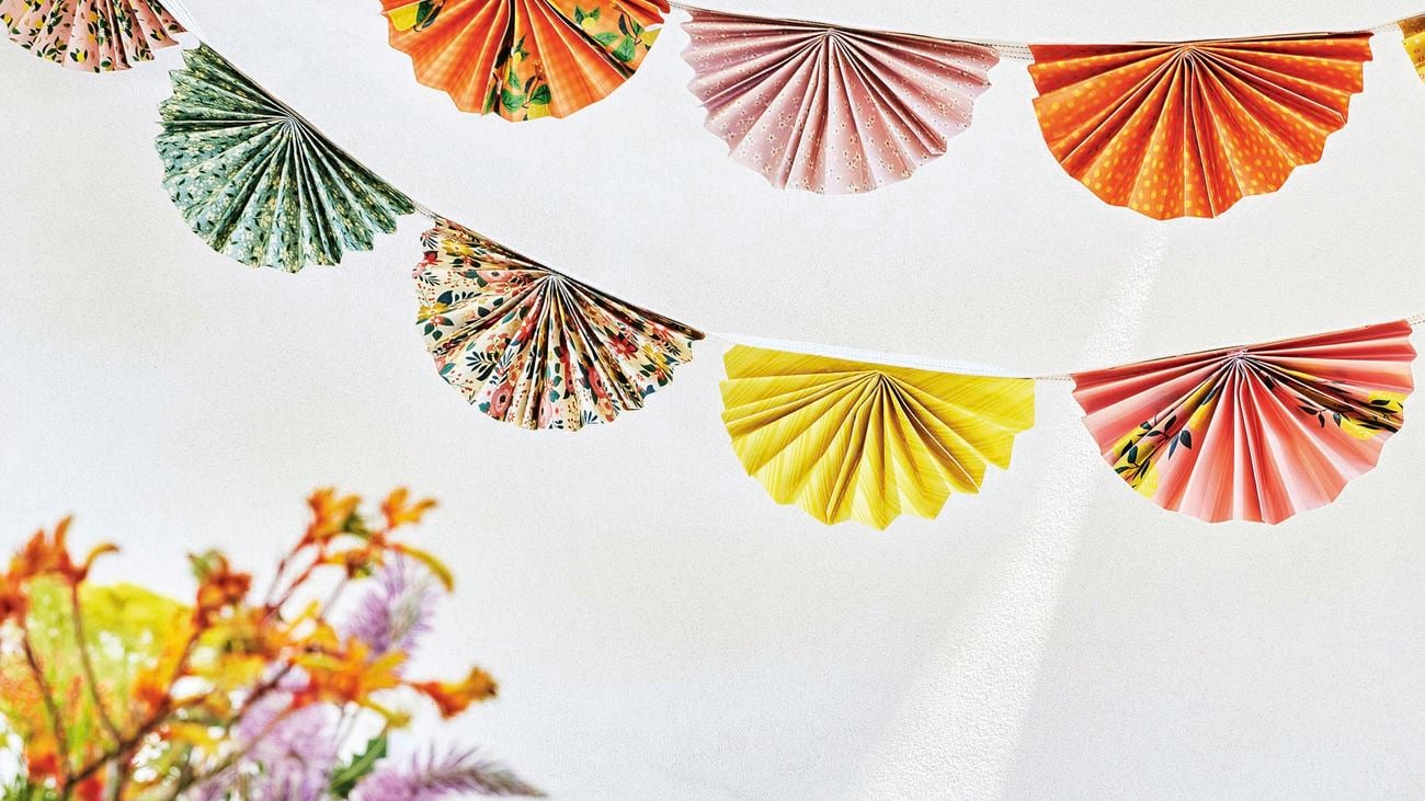 Two strings of paper decorations hang above a dining table set up with colourful vases and flowers.