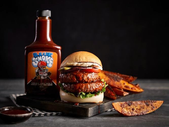A burger with sweet potato and sauce bottle on a chopping  board.