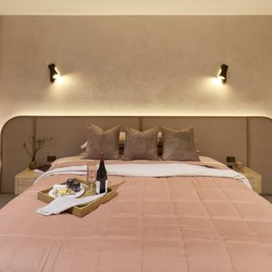 Contemporary bedroom featuring soft pink bedding, a curved upholstered bedhead, neutral walls and wall-mounted bedside lights.