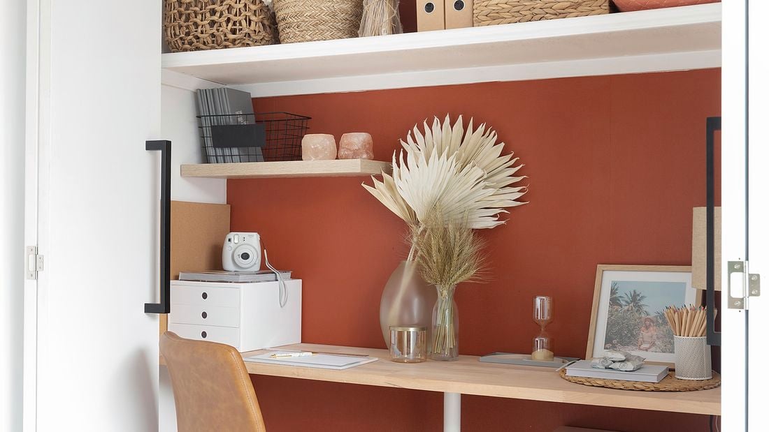 Renovated home office with burnt orange walls, desk built into cupboard and floating shelves.