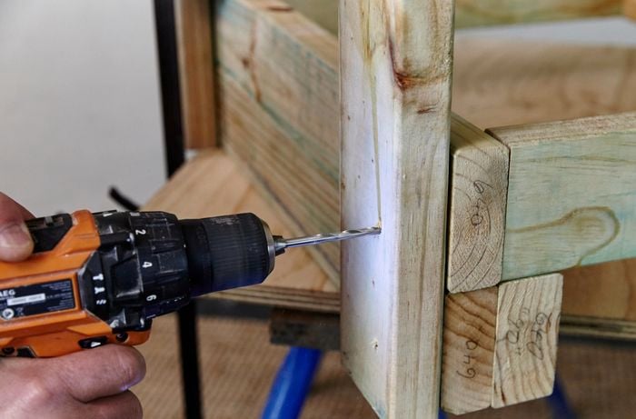 A person drilling a hole in a length of pine framing timber