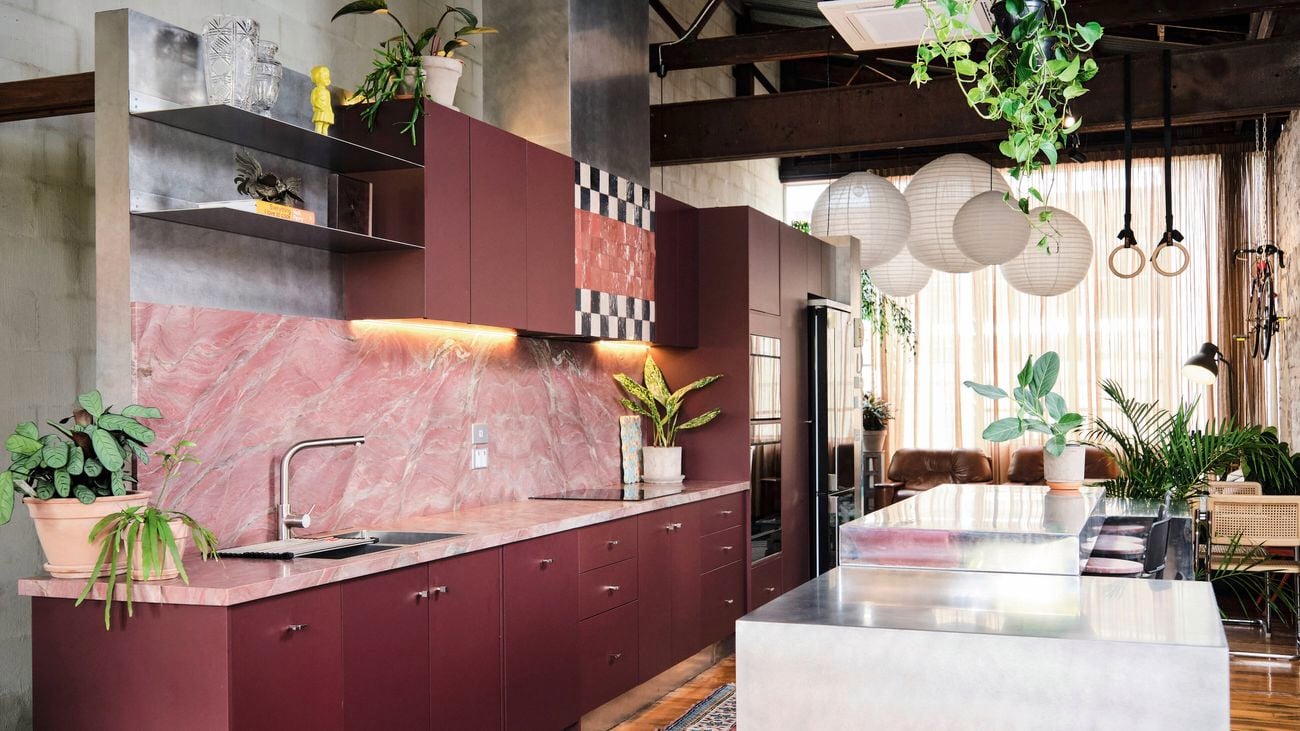 Modern kitchen with maroon cabinetry, pink natural stone splashback and benchtop, and a black and white checkered accent